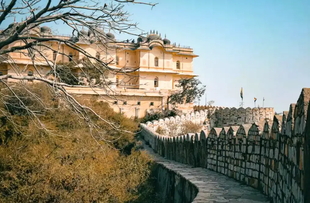 Nahargarh Fort's stone defensive wall walkway curving toward the palace complex with Indian flags and dry Aravalli hillside, Jaipur
