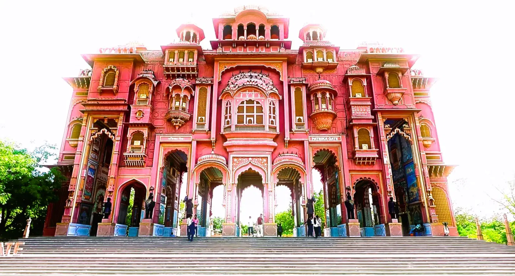 Front view of Patrika Gate's ornate rose-pink Rajasthani facade with wide staircase and intricate carved detailing at Jawahar Circle, Jaipur