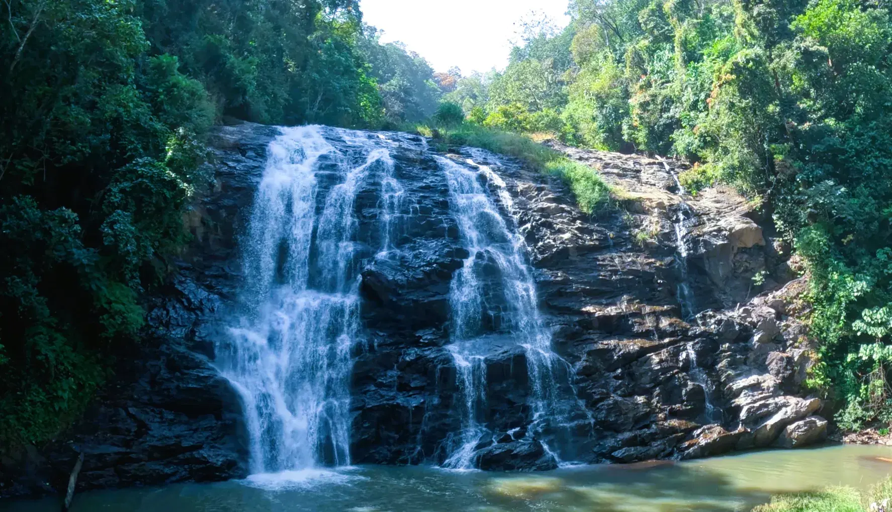 Abbey Falls flowing over a broad rock face amid dense forest near Madikeri