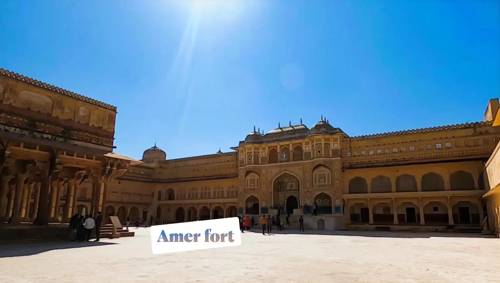 Amber Fort's inner courtyard with ornate Ganesh Pol gateway, colonnaded arches, and tourists on the marble floor, Jaipur