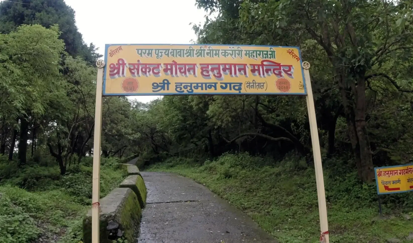 Entry gate and pathway leading to Hanuman Garhi temple on a forested hilltop in Nainital